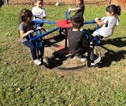 Children playing on a colorful merry-go-round in a grassy playground.